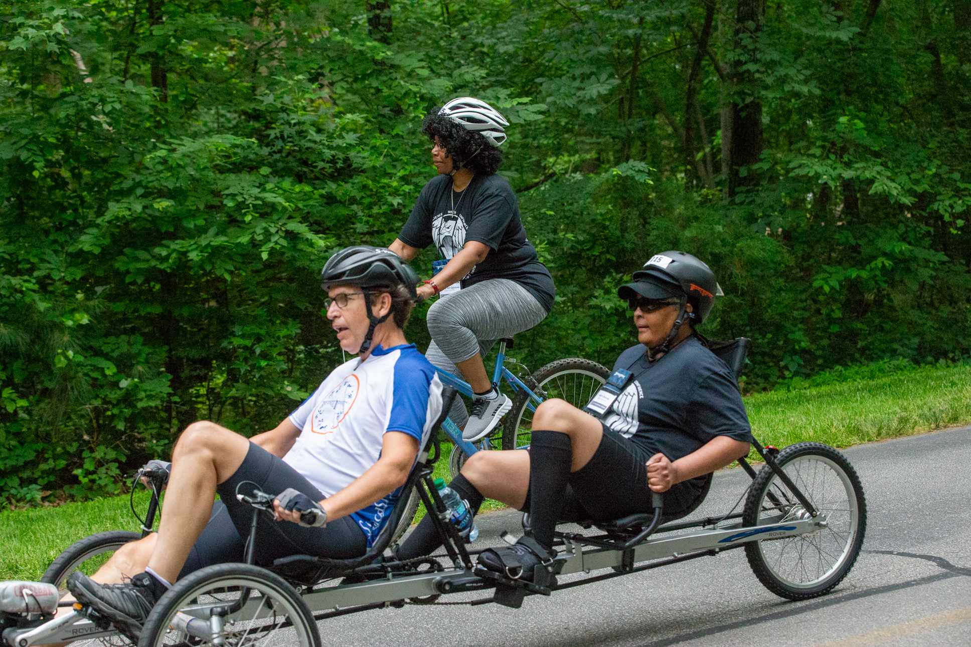 Athletes pedaling a tandem recumbent cycle with an athlete pedaling an upright cycle