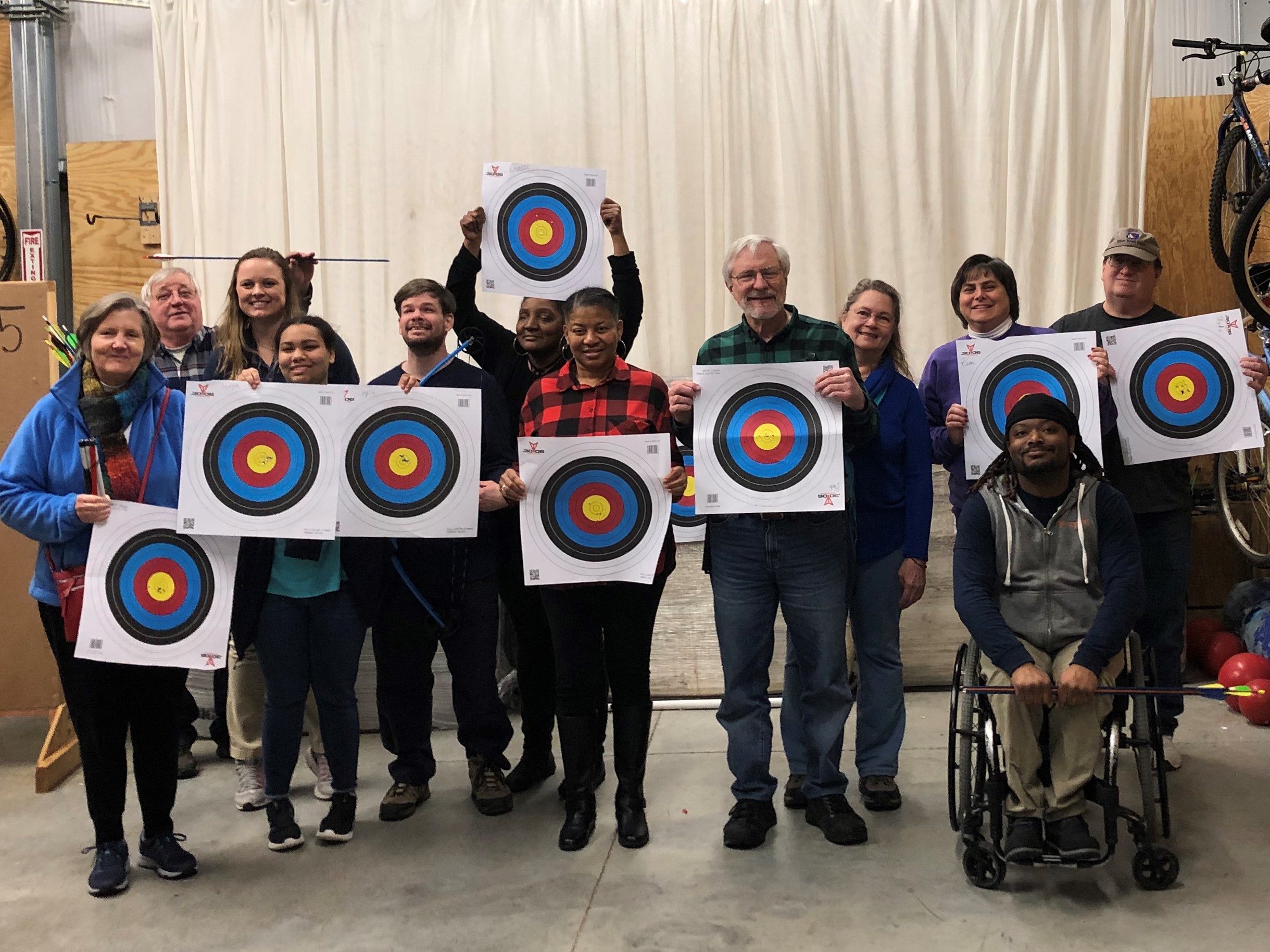 Group of athletes with visual impairments holding up archery targets with Bridge 2 Sports staff and coaches
