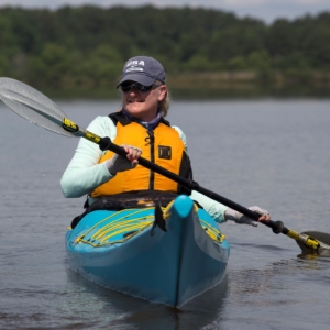 ashley thomas paddling in a blue kayak on lake crabtree