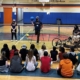 Wes Hall, man with right leg amputation, stands in front of middle school students seated on gym floor