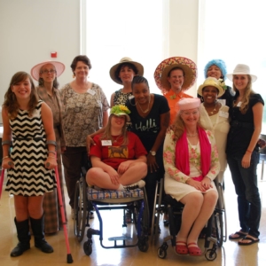 group of women and girls some using wheelchairs and forearm crutches smile in group wearing fancy hats at GiGe event in 2014