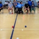 athlete in wheelchair plays boccia with college students from Duke sitting next to her