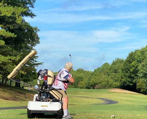 with blue sky above and man hits a drive on golf course from a solo rider adapted cart